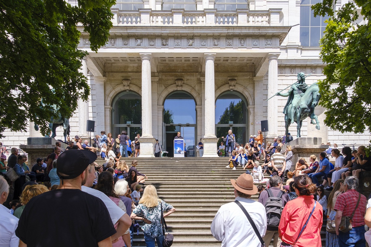 Jahresausstellung 2023 vor dem Eingang der AdBK München. Zu sehen sind viele Besucher, die vor und auf der Treppe  stehen. 